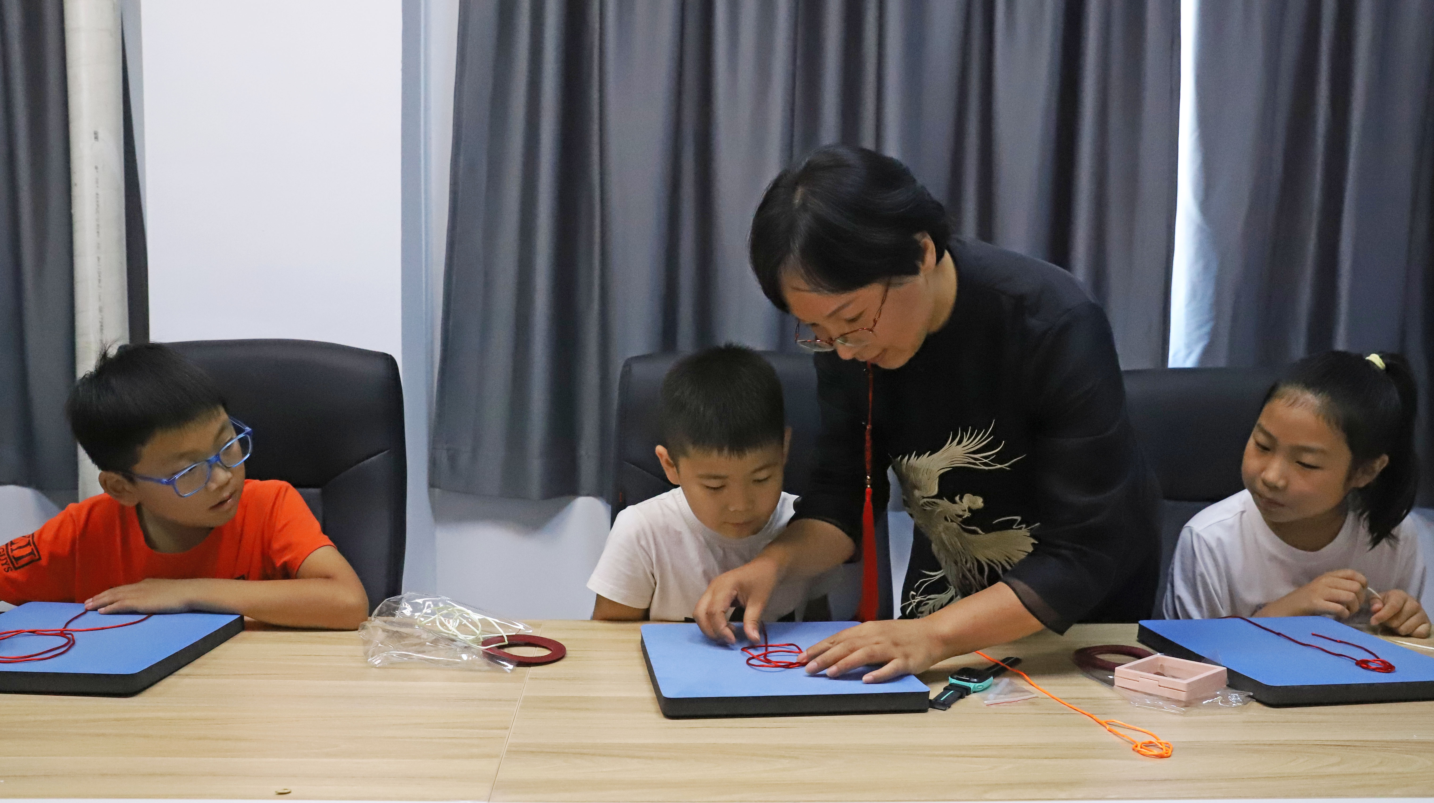 河北涿州:学生们假期生活增添“非遗色”_fororder_7月16日,涿州市非遗人传承人于长娟指导学生编织绳结。熊华明摄