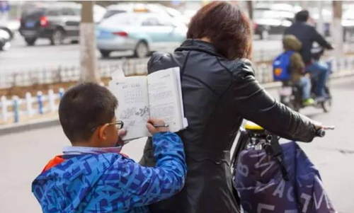 4 早晨,一位看上去只有一二年级的小学生趴在妈妈后背上看书学习.