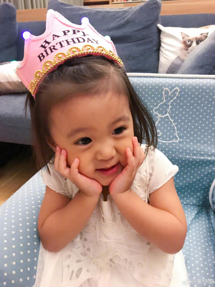 两岁的咘咘身穿白色公主裙,戴着生日帽,双手托腮,表情甜甜像足小