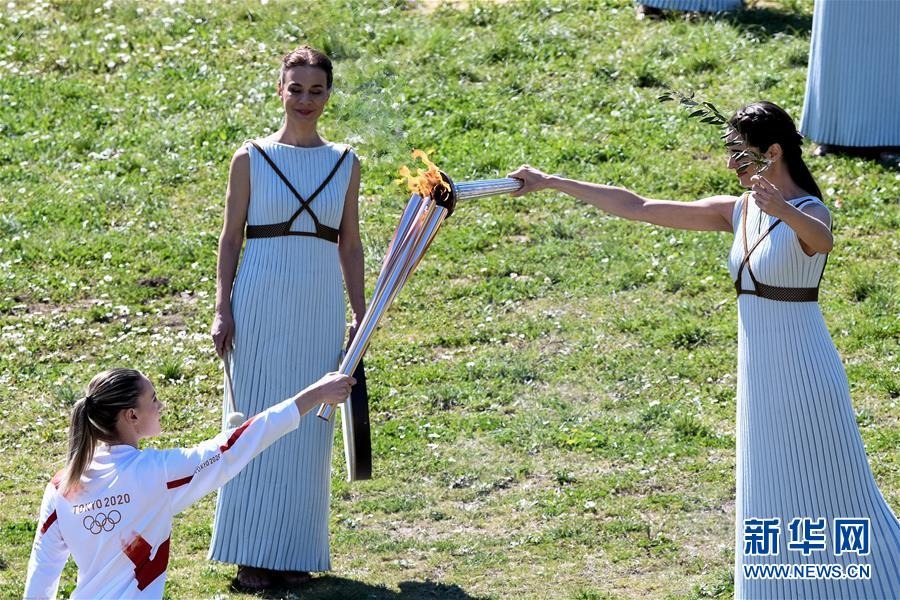 3月12日，第一棒火炬手、希腊射击奥运冠军安娜·克拉卡奇（左）与扮演最高女祭司的演员乔治乌（右）交接圣火。 当日，2020东京奥运会圣火采集仪式在希腊古奥林匹亚举行。 新华社发（安东尼斯·尼科洛普洛斯摄）