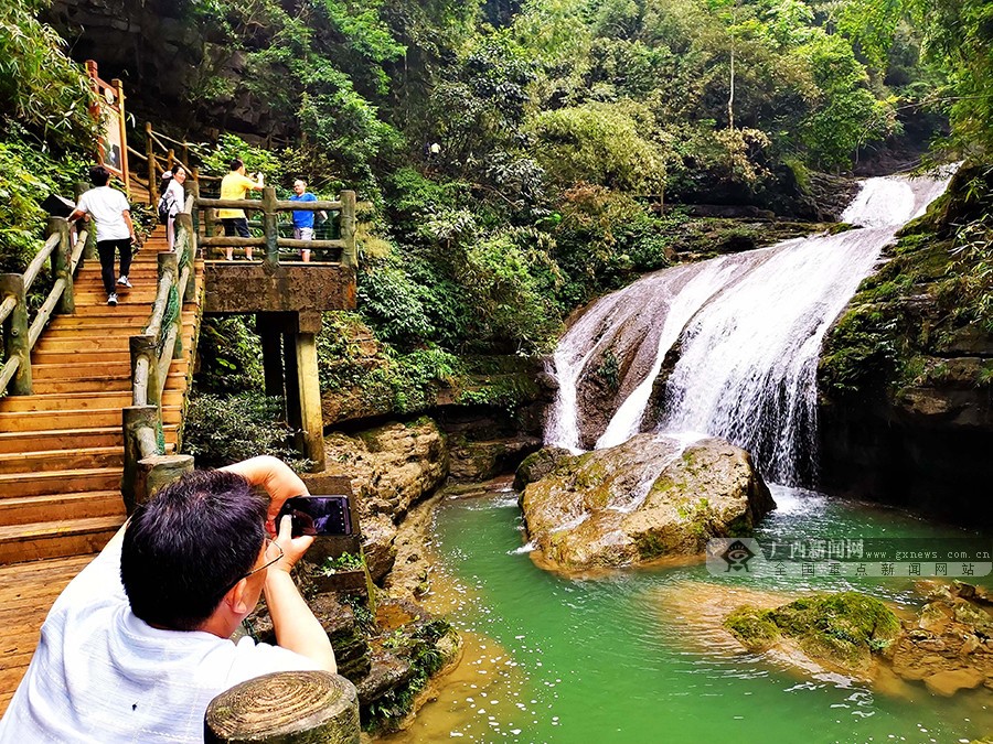 圖片默認標題_fororder_圖為5月12日，遊客在環江毛南族自治縣牛角寨景區的“三疊泉”瀑布遊玩拍照。高東風攝