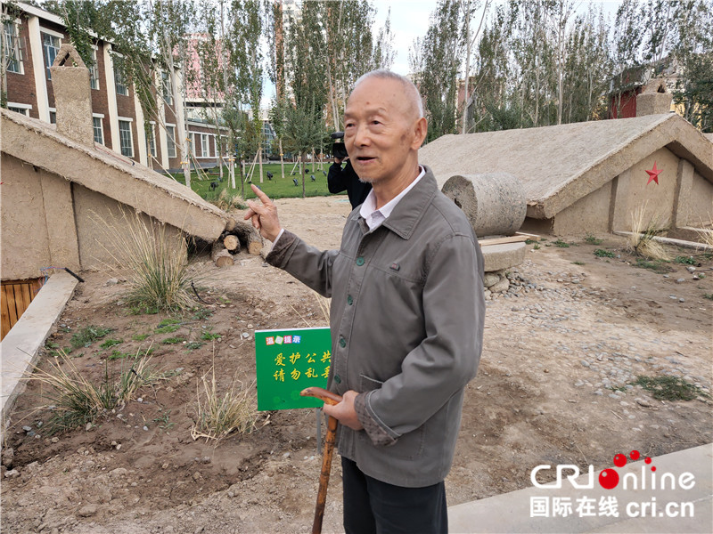 【续写丝路新篇章】新疆兵团军垦博物馆：不忘来时路 不罔肩头担（组图）_fororder_06记者在新疆兵团军垦博物馆偶遇的阎姓老人，他正在给围观过来的群众讲解过去的地窝子。老人来自河南周口，1958年来到新疆支援建设。老人说地窝子在当时是冬暖夏凉的一种建筑，但是和现在有暖气空调的楼房没法比。现在石河子到处都是楼房，地很平整，群众的生活水平提高了，可是比以前好很多。（地窝子是新疆生产建设兵团在当时沙漠化的土地上给自己建造的简陋住所，在平地上挖个坑，再搭上简单的顶，就是一个地窝子。） 摄影：位树理