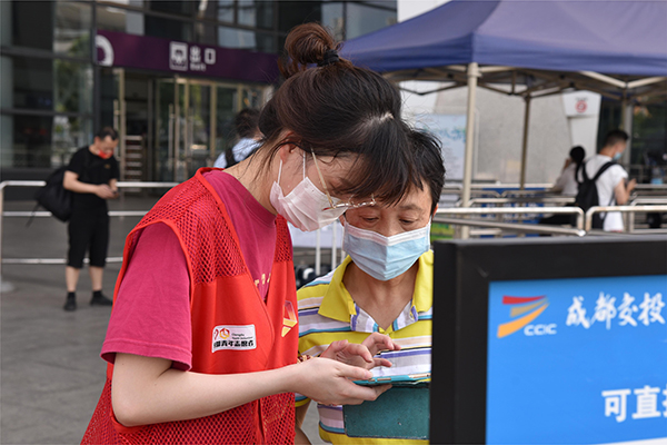 直面高温“烤”验 坚守交通一线——致敬高温下的文明交通守护者_fororder_客运场站的志愿者帮助旅客完成扫码-供图-成都市交通运输局