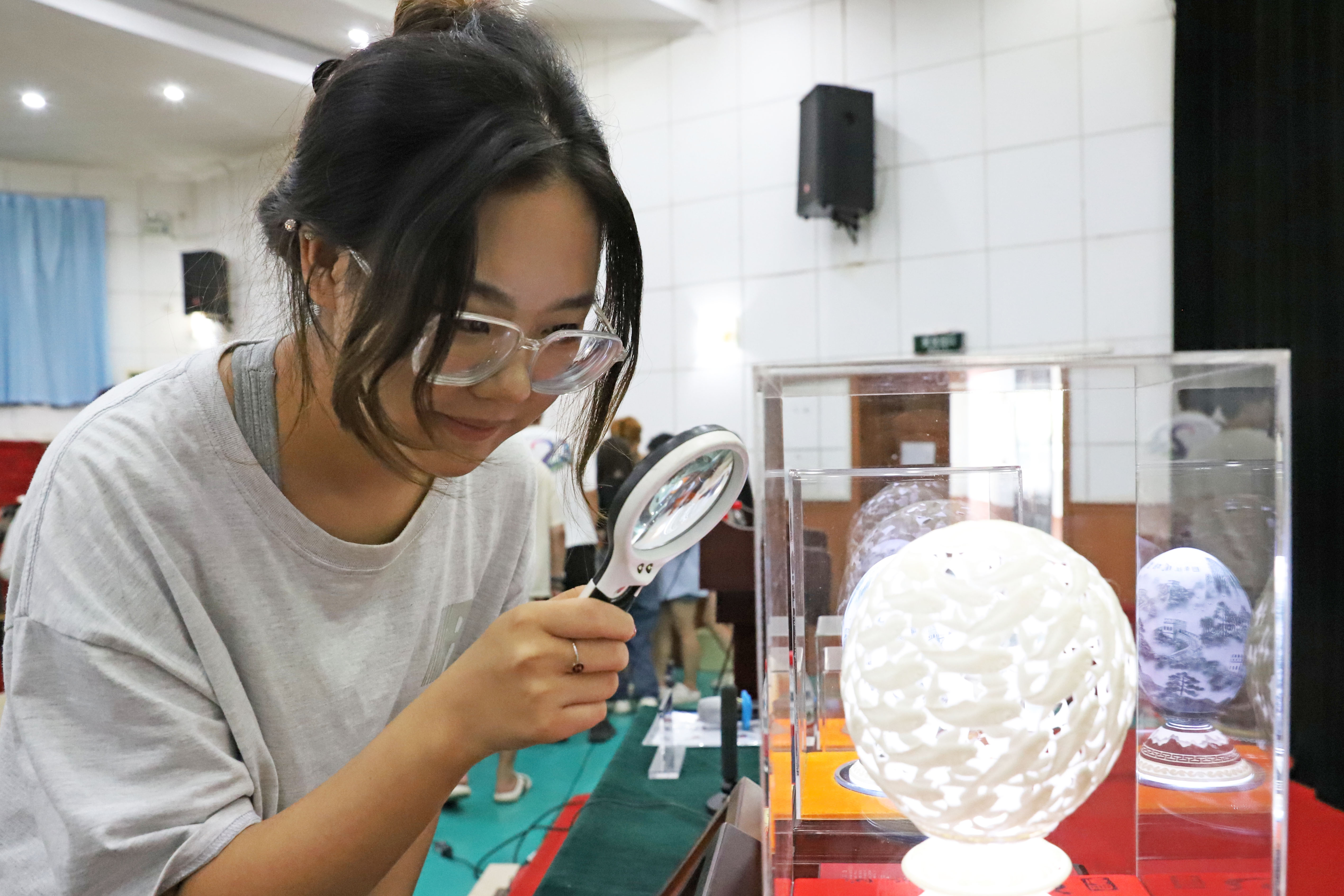 河北涿州：非遗项目搬进高校教室_fororder_7月5日，北京财贸职业学院涿州分校，学生使用放大镜观看蒲德荣的蛋雕作品。熊华明摄