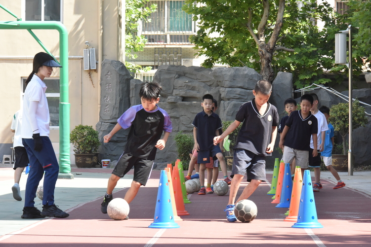 石家庄裕华区6所小学开启暑期托管_fororder_阳光小学的学生们在老师的带领下进行带球绕桩训练.JPG
