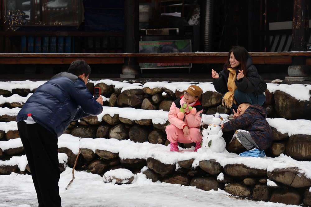 貴州雷山西江千戶苗寨迎來降雪  冬日雪景如畫_fororder_1月22日，貴州省雷山縣西江千戶苗寨迎來2024年第一場降雪。圖為遊客在合影留念。